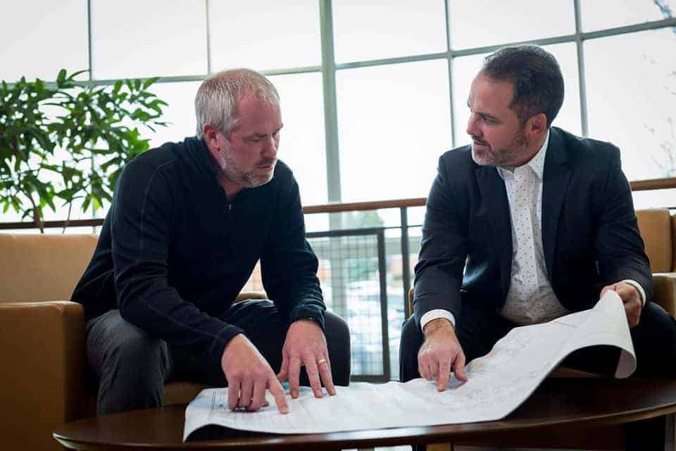 Two men examining blueprints for a roofing project