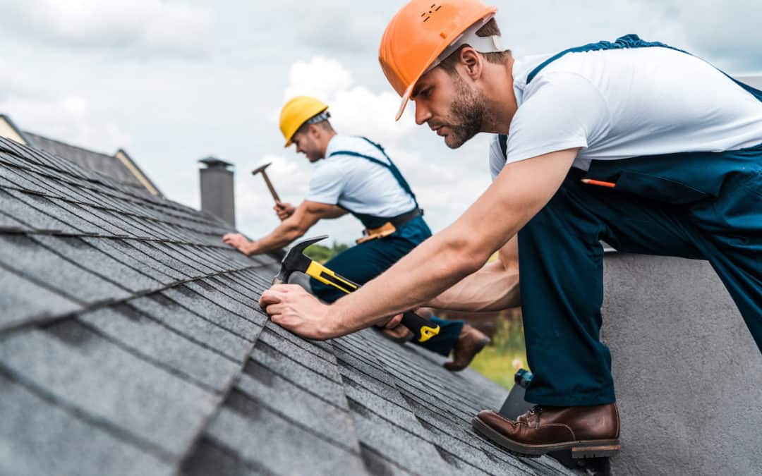 two men with hard hats repairing a roof on a cloudy day